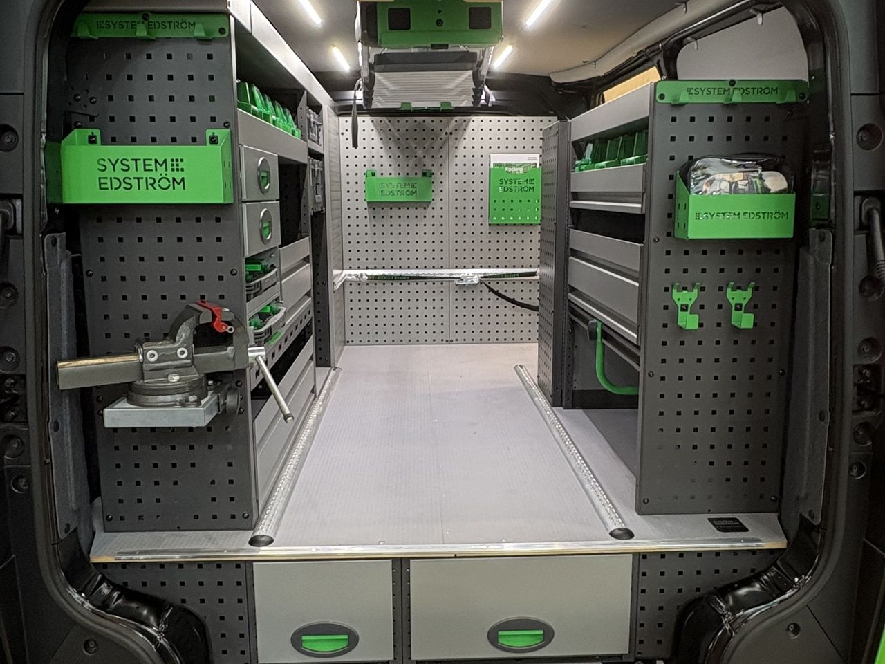 Intérieur d'un Kia PV5 Cargo L2H1 aménagé, vu depuis les portes arrière : étagères métal sur les deux parois et caisson à tiroirs sous plancher
